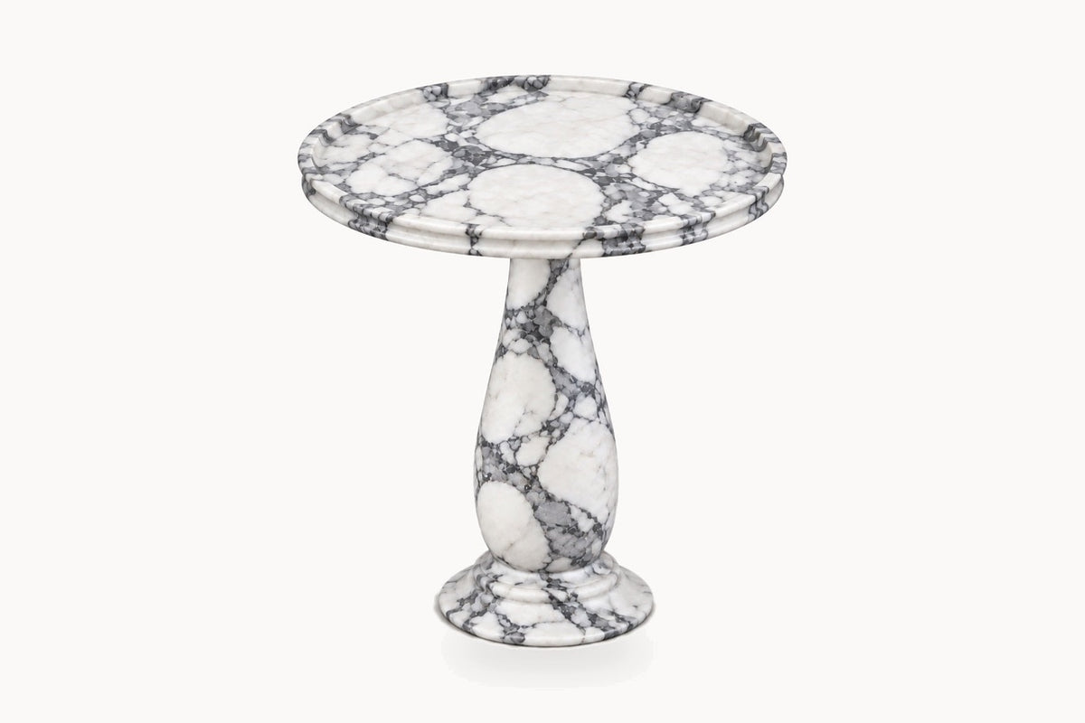 A round pedestal side table made of white marble with prominent gray and black veining, shown on a plain off-white background.