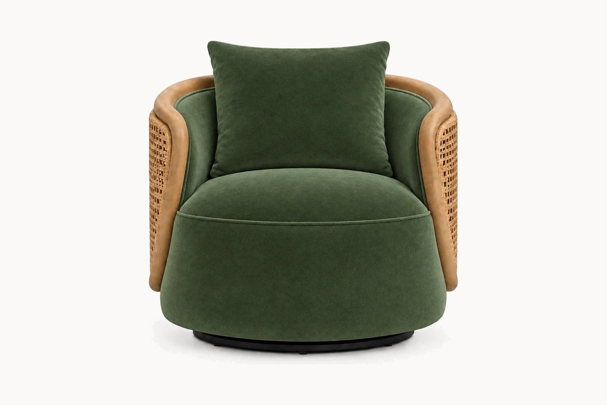 A modern barrel-style accent chair upholstered in deep green velvet with a matching back cushion, featuring natural woven rattan armrests and a black circular base, shown against a plain white background.